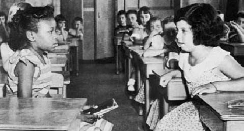 Black and white girls looking at each other in a classroom. Probably in the late 1950s.